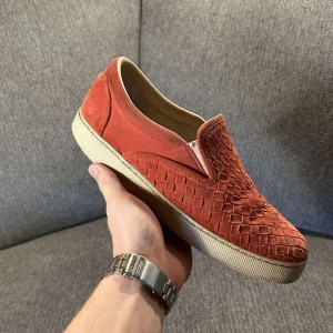  Bottega Veneta - Säljer ett par röda slip-on sneakers från Bottega Veneta i lyxig mocka med deras ikoniska flätade mönster. Skorna har vit platt sula och rund tå, samt en snygg och stilren design som sticker ut. Perfekta för dig som gillar exklusiva detaljer och italiensk känsla. Priset kan diskuteras 😊