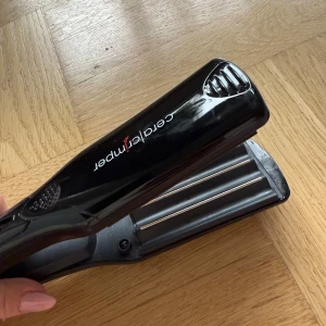Cera Crimper - Cera Crimper är en professionell vågtång för håret med keramiska plattor. Ger snygga vågor och volym. Svart design, synligt i gott skick utan större repor eller slitage. Enkel att använda med on/off-knapp och greppvänligt handtag. Perfekt för styling hemma.