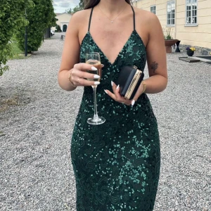 Grön balklänning från Dressoom linne  - Säljer en smaragdgrön långklänning med tunna axelband och djup v-ringning. Klänningen är täckt av glittrande paljetter och har ett vackert mönster över hela tyget. Den är figurnära och har öppen rygg nypris är 6 000 kr endast använd en gång 