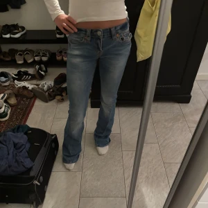 True Religion ljusblå bootcut jeans - Ljusblå jeans från True Religion med klassiska kontrastsömmar och broderade bakfickor. Köpta för 1699, säljer för 400 då de är något slitna vid fickan och har två mindre hål vid hälarna