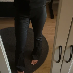Svarta bootcut byxor med glansig finish - Säljer ett par svarta byxor med glansig finish och bootcut-modell. Byxorna har klassisk femficksdesign, normal passform och midd midja. Perfekta för dig som vill ha en stilren look med lite edge. Storleken är L/34