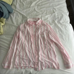 Rosa och vit randig skjorta Victoria's Secret - Söt skjorta från Victoria's Secret i rosa och vitt med breda ränder. Klassisk krage, knäppning framtill och lång ärm. Insidan av kragen har ett gulligt prickigt mönster. Skjortan är i mjuk bomull och har en bröstficka. Liten fläck som visas på sista bilden. 