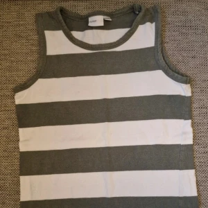 Randigt linne - Linne från my wear young med breda horisontella ränder i grönt och vitt. Toppen har rund halsringning och är tillverkad i mjuk bomull, perfekt för varma dagar. Enkel och stilren design som passar till det mesta. Det är en liten prick på linnets framsida (se bild) och det har varit tvättat såpass många gånger att färgen har blivit påverkad (se bild). Inga andra skavanker vad jag har sett. Stl 134/140 