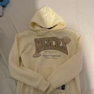 Off white hoodie från Mercier - Säljer en off white hoodie från Mercier med stor logga framtill. Tröjan har huva, känguruficka och är tillverkad i en mjuk mix av bomull och polyester. Perfekt för dig som gillar streetwear och vill ha en chill look.funkar också för storlek M och är i underbart skick