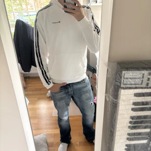 Vit hoodie från Champion med svarta detaljer - Vit hoodie från Champion med svarta ränder och logotyper längs ärmarna. Klassisk huva, känguruficka och långärmad modell. Perfekt för dig som gillar sportig och clean stil.