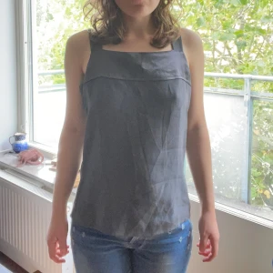 Grå axelbandtopp y2k - En stilren grå topp från Number One by KappAhl. har breda axelband och rak passform, perfekt för en enkel och clean look. Materialet har en lätt glansig yta som ger en snygg touch. Passar dig som gillar minimalistisk stil.