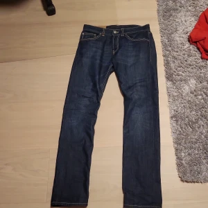 Mörkblå jeans från Dondup, stl 31 - Snygga mörkblå jeans från Dondup i klassisk femficksmodell. Jeansen har raka ben, kontrastsömmar och normal passform. Tillverkade i slitstarkt denimtyg som ger en stilren look. Perfekta för dig som gillar en enkel men trendig stil.