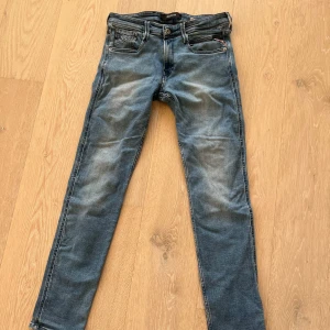 Replay blå jeans, modell Waitom W29 L32 - Snygga blå Replay Waitom jeans med klassisk femficksdesign och coola slitningar. Jeansen har raka ben, normal passform och detaljerade bakfickor. 
