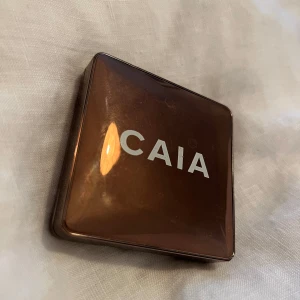 CAIA Glow Bronzer Gold Coast - Snygg bronzer från CAIA i nyansen Gold Coast. Kommer i en brun, fyrkantig dosa med spegel i locket. Ger en varm, solkysst look med en lätt glow. Perfekt för att framhäva ansiktsdragen och skapa dimension. Praktisk dosa i plast, enkel att ta med i väskan.