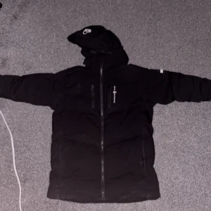Svart Sail racing jacka - Svart pufferjacka från Zalando med huva och hel dragkedja framtill. Jackan har två sidofickor med dragkedja och en bröstficka. Perfekt för kalla dagar med sin vadderade design och stilrena look.köpte den för 4,5tusne från Zalando 6 månader sen