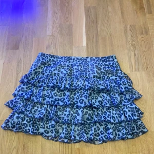  Grå leopardmönstrad volangkjol, M -  Är osäker på storlek men skulle gissa på M. Säljer en  volangkjol med leopardmönster i svart och grått. Kjolen har flera lager volanger.