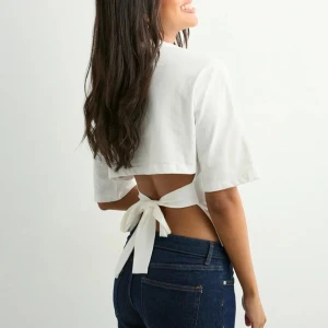 Vit topp med knyt i ryggen Nelly  - Säljer en vit croppad topp med korta ärmar och rund hals. Toppen har öppen rygg med breda band som knyts i en rosett bak, vilket ger en snygg och trendig look. Perfekt för varma dagar och att styla med jeans eller kjol.