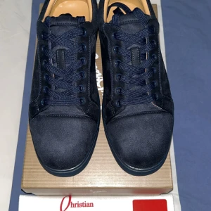 Mörkblå sneakers från Christian Louboutin - Snygga mörkblå sneakers från Christian Louboutin i mocka med klassisk röd sula. Skorna har rund tå, platt sula och snörning. Perfekta för dig som vill sticka ut med exklusiva detaljer och lyxig känsla.