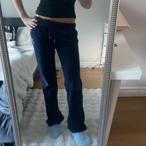 Juicy Couture mörkblå mjukisbyxor XXS - Mörkblå mjukisbyxor från Juicy Couture i velour med snörning i midjan och glittriga stenar som bildar texten 'Juicy' på baksidan. Byxorna har normal passform och är perfekta för en chill och trendig look.