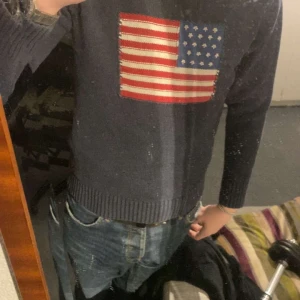 Mörkblå Gant tröja med USA-flagga - Säljer en mörkblå tröja från Gant i 100% bomull med en stor broderad amerikansk flagga på bröstet. Tröjan har ribbade muddar och rund hals. Perfekt för dig som gillar klassisk preppy stil och vill sticka ut lite extra. Är liten i storleken så sitter mer som en S 