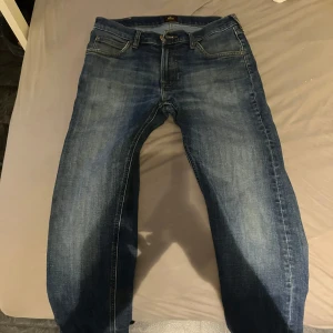 Blå jeans från Lee med raka ben - Säljer ett par klassiska blå jeans från Lee med raka ben och snyggt slitna detaljer. Jeansen har fem fickor, normal passform och Lee-logga på bakfickan. Perfekta för dig som gillar en tidlös och avslappnad stil. I storlek S 