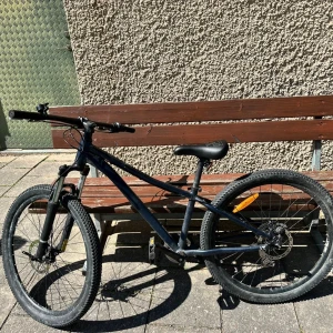 Helt ny cykel 24 tum - Bilderna visar en svart mountainbike med grova däck, skivbromsar och sportig ram. Cykeln ser ut att vara i gott skick med mindre tecken på normalt slitage, främst på däcken och ramen. Perfekt för både stadskörning och terräng. Sadel och styre ser bekväma ut.