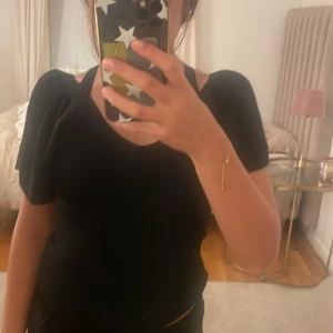 Svart ribbad topp med puffärm från Only - Svart ribbad topp från Only med v-ringning, korta puffärmar och snygga knytband i ryggen. Toppen har en figurnära passform och är tillverkad i stretchigt material som sitter skönt. Perfekt för dig som gillar trendiga detaljer och stilren look. Andvänt ändas 2 tillfälle.