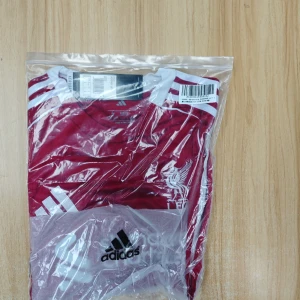 Liverpool FC Adidas matchtröja röd S - Liverpool FC matchtröja från Adidas i rött med vita detaljer och loggor. Slim fit-modell med korta ärmar, tillverkad i lätt och ventilerande material. Klassiska Adidas-ränder på axlarna och klubbmärke på bröstet. Perfekt för dig som älskar fotboll och vill visa ditt stöd.