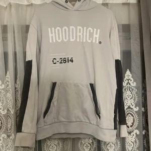 Grå hoodie från Hoodrich med tryck - Snygg grå hoodie från Hoodrich med stora vita tryck fram och bak, samt svarta detaljer på ärmar och fickor. Hoodien har huva med metallöljetter, känguruficka och cool världskarta-tryck på ryggen. Perfekt för dig som gillar streetwear.