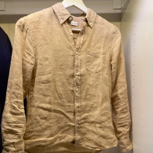 Beige linneskjorta från Gant 146/152cm - Snygg beige linneskjorta från Gant. Klassisk button-down krage, bröstficka med diskret text. Perfekt för en chill och stilren look. Långärmad och med avslappnad passform. Mvh Hannes!