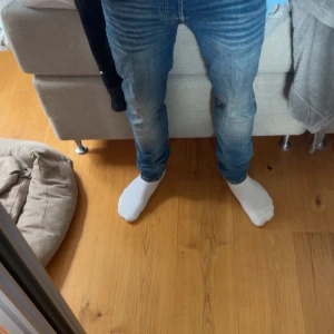 Blå jack&jones jeans - Snygga blå jeans från jack&jones i modellen slim/genn fit. Jeansen har klassisk femficksdesign, normal midja och smal passform längs benen. Materialet är mjukt denim i bomull och de har en lätt tvättad look med subtila slitningar. Perfekta för en stilren och modern vardagsstil.