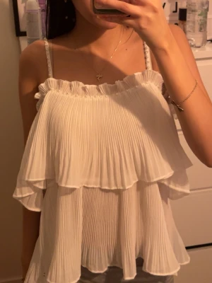 Vit volangtop  - Säljer en superfin topp från Chica London med tunna axelband dekorerade med små pärlor. Den är i storlek L men se på bilden för att se hur den sitter på mig som använder XS/S