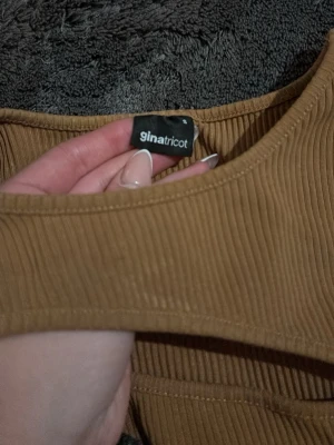 Ribbad långärmad topp Gina Tricot - Säljer en snygg ribbad långärmad topp från Gina Tricot i en varm beige färg. Toppen har en unik detalj med en vågig söm över bröstet och är tillverkad i ett mjukt stretchigt material. Perfekt att styla med jeans eller kjol!