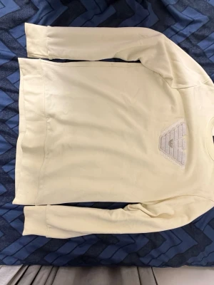 Beige sweatshirt från Emporio Armani - Säljer en beige sweatshirt från Emporio Armani med broderad logga framtill i vitt och beige. Tröjan har rund halsringning, långa ärmar och ribbade muddar vid ärmslut och nederkant. Perfekt för dig som gillar stilrena och exklusiva plagg.