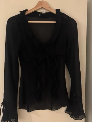 Svart blus - Svart blus med snören på framsidan och ärmarna, passar mig som har storlek S.
