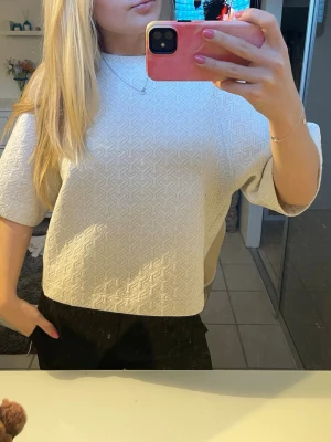 Vit mönstrad topp från Kappahl - Säljer en vit topp från Kappahl i storlek S. Toppen har ett geometriskt mönster i tyget med guld detaljer, boxig passform och korta ärmar. Materialet känns mjukt och lite tjockare, perfekt för dig som gillar stilrena men ändå unika plagg.