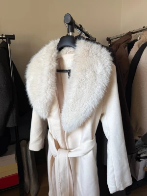 Vit kappa med fuskpäls från H&M - Säljer en lång, vit kappa från H&M med fuskpäls. Använd 1-2 ggr som ny. 