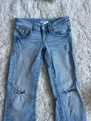 Ljusblå jeans från Gina Tricot - Säljer ett par ljusblå jeans från Gina Tricot i storlek 140. Jeansen har slitna detaljer vid knäna och klassisk femficksdesign. Tillverkade i mjukt denimtyg med raka ben och knappgylf. Perfekta för en avslappnad och trendig look.