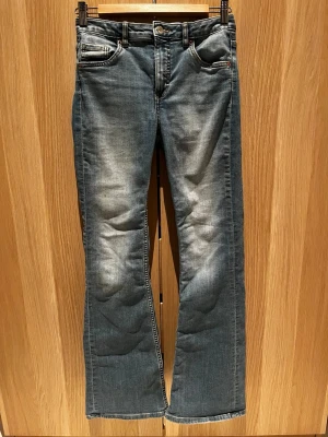 Blå raka jeans från Kappahl, stl 164 - Snygga blå jeans från Kappahl i rak modell med klassisk femficksdesign. Jeansen har en lätt tvättad look och normal passform. Tillverkade i mjukt denimtyg med bälteshällor och knappstängning. Perfekta för en chill vardagsstil.