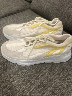 J.Lindeberg vita och gula sneakers - Snygga sneakers från J.Lindeberg i vitt och gult med mesh och mockadetaljer. Skorna har en chunky sula, snörning och coola gula detaljer längs sidan samt logga bak på hälen. Perfekta för dig som vill ha en sportig och fräsch look.