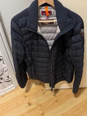 Svart lättviktsjacka från Parajumpers  - Svart lättviktsjacka från Parajumpers med quiltad design och hög krage. Jackan har dragkedja framtill, två sidofickor med dragkedja och en patch på ärmen. Jackan är svart och nsidan är ljusgrå. Perfekt för kyliga dagar. Storlek XXL men passar en XL/L. 