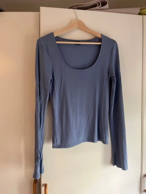 Blå långärmad topp från Gina Tricot - Säljer en ljusblå långärmad topp från Gina Tricot i storlek L. Toppen har en djup rundad halsringning och är tillverkad i mjuk bomull. Ärmarna har en liten slitsdetalj vid mudden som ger en extra touch. 