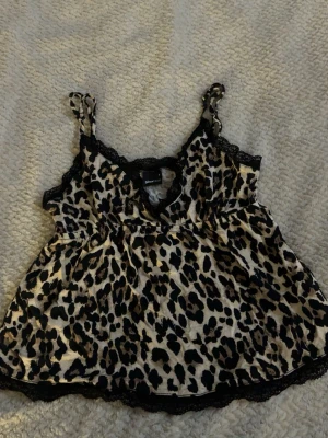 Leopardmönstrad linnetopp Gina Tricot - Säljer en leopardmönstrad linnetopp från Gina Tricot i storlek S. Toppen har tunna axelband, spetsdetaljer vid halsringningen och nederkanten samt en lös passform. Perfekt för dig som vill sticka ut med ett djurmönster.