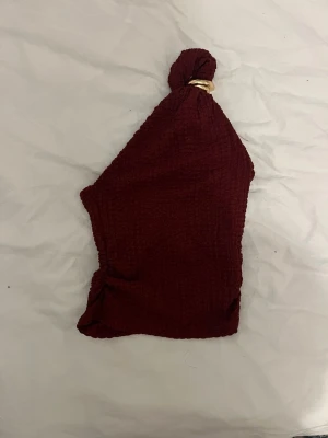 Vinröd oneshoulder topp från H&M - Säljer en vinröd oneshoulder topp från H&M,  toppen har en snygg guldfärgad detalj vid axeln och är croppad med en tight passform. 