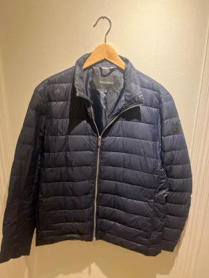 Mörkblå pufferjacka från Matinique - Säljer en mörkblå pufferjacka från Matinique i storlek S. Jackan har quiltad design, dragkedja framtill och en snygg logodetalj på ärmen. Tillverkad i syntetmaterial och perfekt för kyligare dagar. Enkel och stilren look som funkar till det mesta.