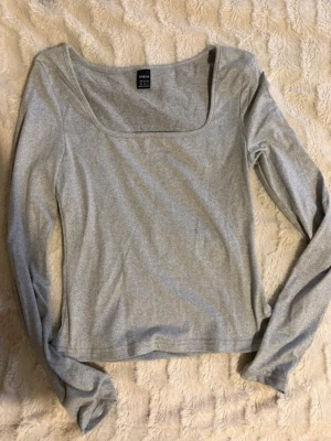Grå långärmad topp från SHEIN - Säljer en stilren grå långärmad topp från SHEIN med fyrkantig halsringning. Toppen är i mjukt och stretchigt material, har en normal passform och är perfekt att matcha med jeans eller kjol. Enkel och snygg design som funkar året runt.