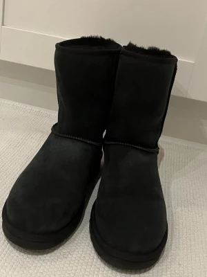 Svarta UGG boots i mocka - Mysiga svarta UGG boots i mjuk mocka med fluffigt foder och platt sula. Klassisk rund tå och diskret UGG-logga bak på hälen. Perfekta för kalla dagar och ger en chill vibe till din outfit. Helt oanvända och sprillansnya uggs. Nypris 3450 kr, pris kan diskuteras.