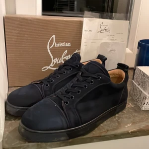 Svarta sneakers från Christian Louboutin - Säljer ett par svarta sneakers från Christian Louboutin med klassisk röd sula och diskret logga på sidan. Skorna har snörning, rund tå och är tillverkade i mocka med detaljer i skinn. Insidan är beige och sulan har den ikoniska Louboutin-signaturen i rött. Kvitto tillkommer såklart. Hör gärna av dig vid funderingar. Mvh Swe Resell