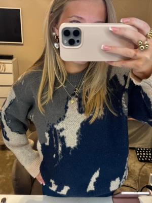 Stickad tröja i blått och grått mönster - Säljer en stickad tröja med coolt abstrakt mönster i mörkblått, grått och beige. Tröjan har rund halsringning och långa ärmar. Perfekt för dig som gillar en chill och trendig stil.