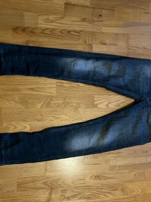 Mörkblå jeans från Nudie Jeans - Säljer ett par mörkblå jeans från Nudie Jeans med klassisk femficksdesign och slitna detaljer vid bensluten. Jeansen har raka ben och tydliga kontrastsömmar. Materialet är robust denim i bomull och passformen är normal.