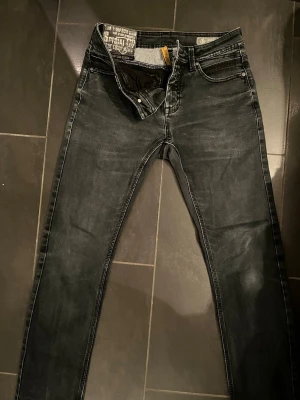 Svarta skinny jeans Tom Tompson - Säljer ett par svarta skinny jeans från Tom Tompson med snygg tvättad look och klassiska fem fickor. Jeansen har normal midja och är tillverkade i stretchigt denim för skön passform. Perfekta till sneakers eller boots.