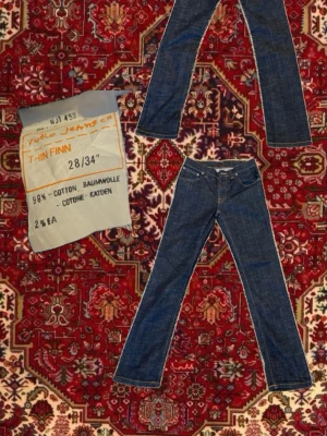 Nudie Jeans Thin Finn blå jeans 28/34 - Säljer ett par klassiska blå jeans från Nudie Jeans, modellen Thin Finn. Jeansen har fem fickor, orange sömmar och är tillverkade i 98% bomull och 2% elastan för lite stretch. Snygg rak passform med smalare ben och normal midja.