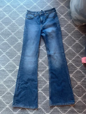 Blå bootcut jeans i storlek 34 - Säljer ett par klassiska blå bootcut jeans i storlek 34. Jeansen har fem fickor, normal midja och är tillverkade i mjukt denimtyg. 
