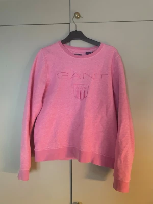 Rosa sweatshirt från GANT - Säljer en rosa sweatshirt från GANT med broderad logga och sköld framtill. Tröjan har rund halsringning, långa ärmar och ribbade muddar. typ nästan aldrig används. Perfekt för dig som gillar en enkel men snygg look.💕💕