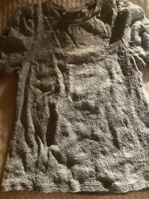 Ljusgrå spetsblus från Kappahl - Säljer en ljusgrå blus från Kappahl i storlek S. Blusen har korta ärmar och är täckt av ett detaljerat spetsmönster som ger en romantisk och cool vibe. Rund halsringning och mjukt material som känns skönt mot huden.